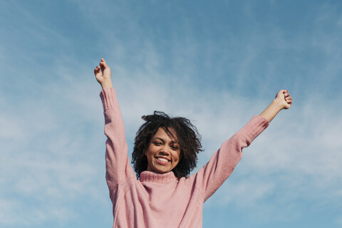 Portrait of smiling young woman against sky raising hands stock photo