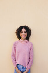 Porträt einer lächelnden jungen Frau mit rosa Pullover, die sich an eine Wand lehnt - LOTF00038