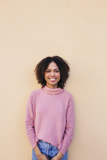 Portrait of smiling young woman wearing pink pullover leaning against wall - LOTF00038