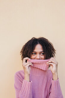 Porträt einer lächelnden jungen Frau, die einen rosa Rollkragenpullover trägt und an der Wand lehnt - LOTF00042
