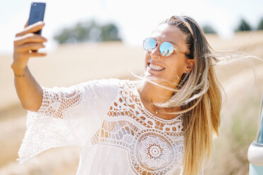 Porträt einer blonden jungen Frau mit verspiegelter Sonnenbrille, die ein Selfie mit ihrem Smartphone macht - OCMF00206