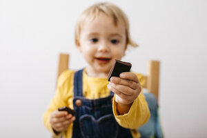 Hand of smiling toddler girl holding piece of chocolate, close-up - JRFF02329