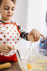 Boy throwing an egg into glass bowl for preparing dough - JRFF02336
