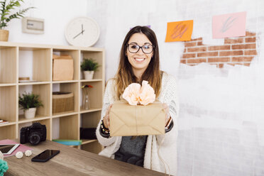 Junge Frau zeigt ein eingepacktes Geschenk in ihrem Atelier - JRFF02378