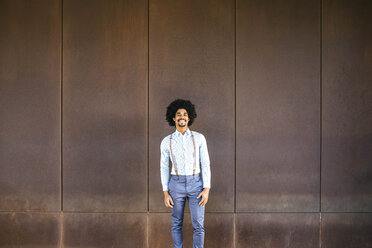 Porträt eines lächelnden Mannes mit Hosenträgern vor einem rostigen Hintergrund - JRFF02394