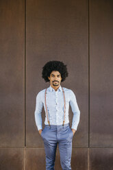 Portrait of bearded man wearing suspenders standing in front of rusty background - JRFF02396