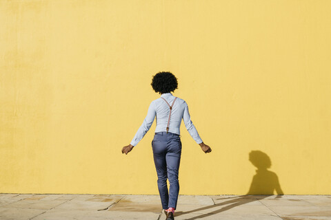 Back view of man wearing suspenders dancing in front of yellow wall stock photo