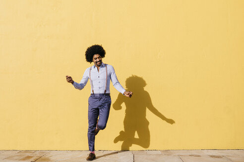 Smiling man dancing in front of yellow wall - JRFF02413