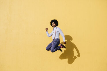 Smiling man jumping in the air in front of yellow wall - JRFF02414