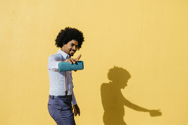 Smiling man with loudspeaker listening music and dancing in front of yellow wall - JRFF02416