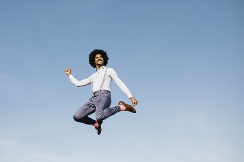 Lächelnder Mann springt in die Luft gegen blauen Himmel - JRFF02424