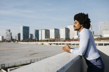 Spain, Barcelona, man leaning on balustrade enjoying sunlight - JRFF02431