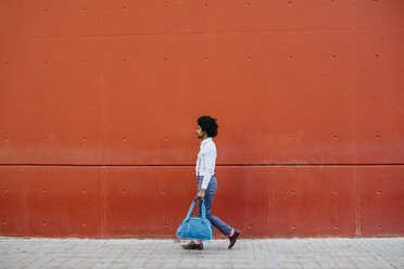 Man with bag walking down the street in front of a red wall - JRFF02438