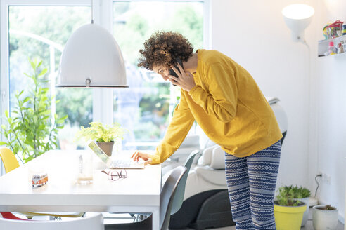 Woman using laptop and cell phone on table at home - JOSF02674