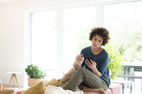 Woman with dog using cell phone at home - JOSF02677