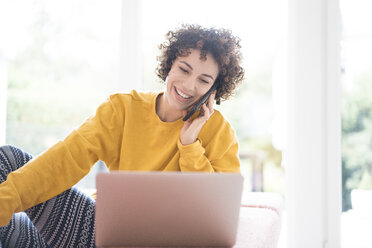 Happy woman using laptop and cell phone at home - JOSF02680