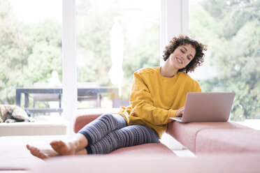 Smiling woman using laptop on couch at home - JOSF02685