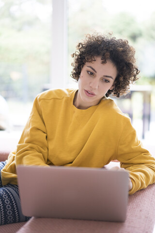 Woman using laptop on couch at home stock photo