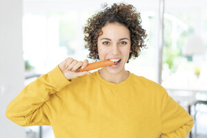 Porträt einer Frau, die zu Hause eine Karotte isst - JOSF02697