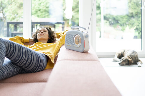 Woman lying on couch listening to music with portable radio at home - JOSF02698