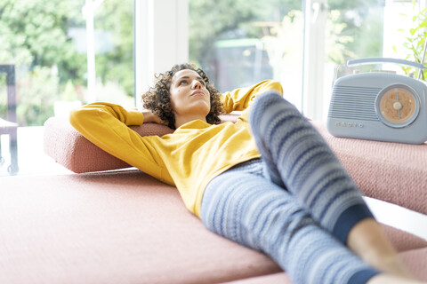 Woman lying on couch listening to music with portable radio at home stock photo