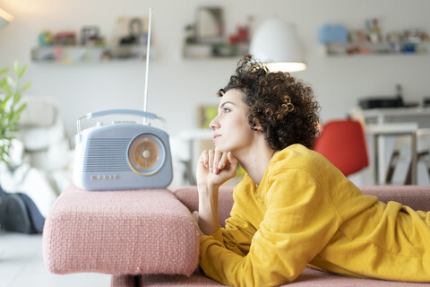 Woman lying on couch listening to music with portable radio at home stock photo