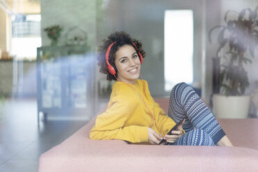 Happy woman listening to music on couch at home - JOSF02702