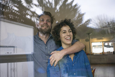 Happy couple behind window at home looking out - JOSF02734