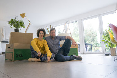 Portrait of couple sitting in living room with cardboard boxes - JOSF02738