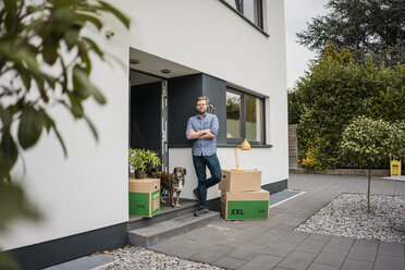 Man with dog standing at house entrance surrounded by cardboard boxes - JOSF02740