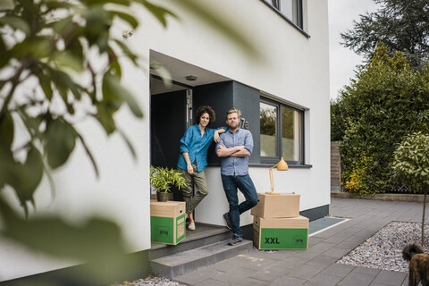 Ehepaar steht mit Kartons am Hauseingang, lizenzfreies Stockfoto