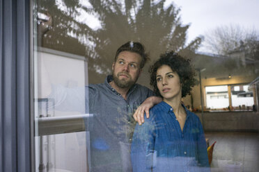 Serious couple behind window at home looking out - JOSF02746