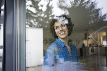 Porträt einer lächelnden Frau zu Hause, die aus dem Fenster schaut - JOSF02747