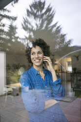 Porträt einer lächelnden Frau am Handy hinter einem Fenster zu Hause - JOSF02748