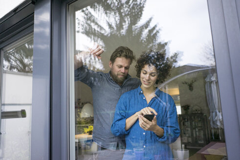 Ehepaar hinter dem Fenster zu Hause beim Telefonieren - JOSF02749