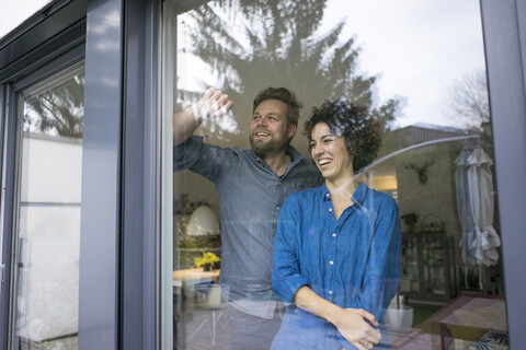 Glückliches Paar hinter dem Fenster zu Hause mit Blick nach draußen, lizenzfreies Stockfoto