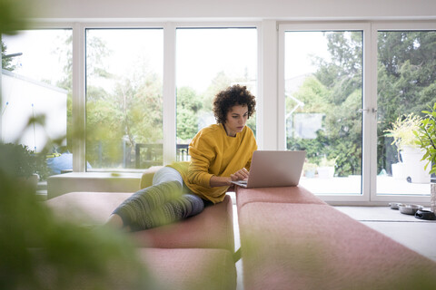 Woman using laptop on couch at home stock photo