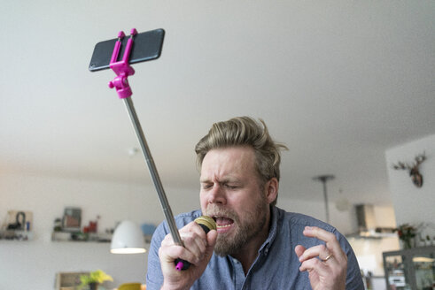 Man at home singing into microphone attached to a selfie stick - JOSF02757