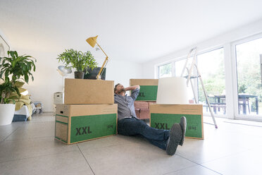 Man sitting on the floor in living room surrounded by cardboard boxes - JOSF02758