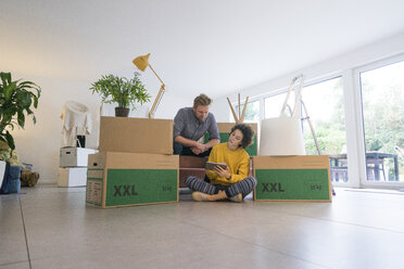 Couple sitting in living room with cardboard boxes using tablet - JOSF02761