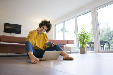 Smiling woman using laptop and tablet at home - JOSF02768