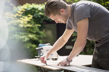 Construction worker measuring wood in driveway - HOXF04230