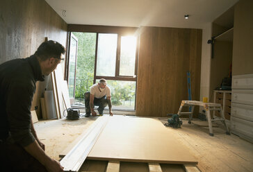 Bauarbeiter messen Holzplatten im Haus aus - HOXF04232
