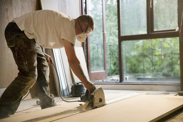 Construction worker using electric saw to cut wood board in house - HOXF04242