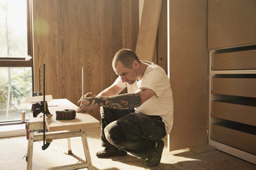 Bauarbeiter mit Tätowierung, der eine Holzplatte in einem Haus misst - HOXF04253