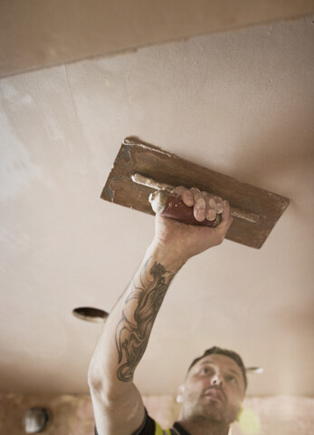 Bauarbeiter mit Tattoo beim Verputzen der Decke, lizenzfreies Stockfoto