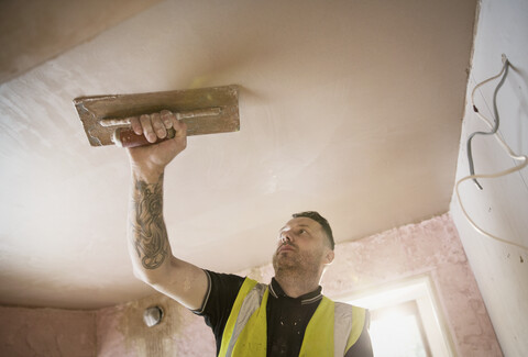 Bauarbeiter mit Tattoo beim Verputzen der Decke, lizenzfreies Stockfoto