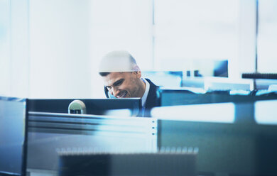 Lächelnder Geschäftsmann, der am Computer im Büro telefoniert - HOXF04277