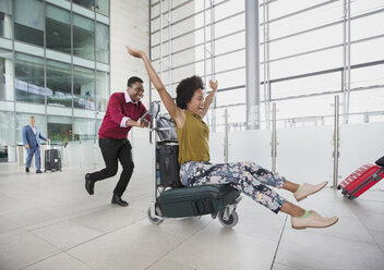 Verspieltes Paar läuft mit Gepäckwagen im Flughafen - HOXF04313