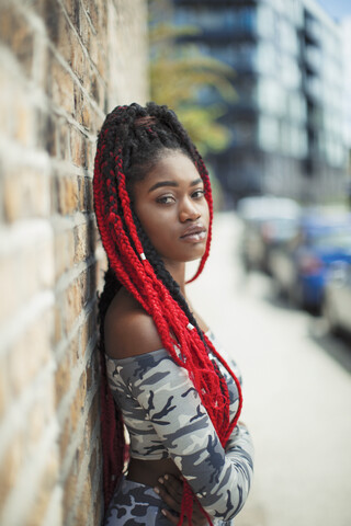 Porträt selbstbewusste junge Frau mit langen roten Zöpfen auf städtischem Bürgersteig, lizenzfreies Stockfoto